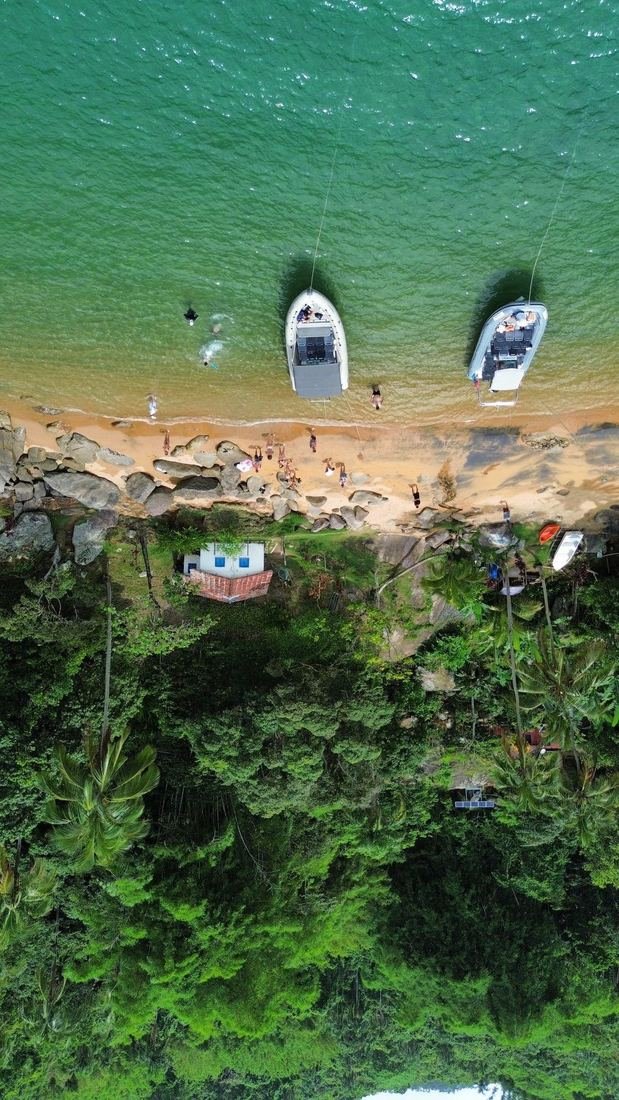 Praia vista de drone, com lanchas ancoradas junto ao costão